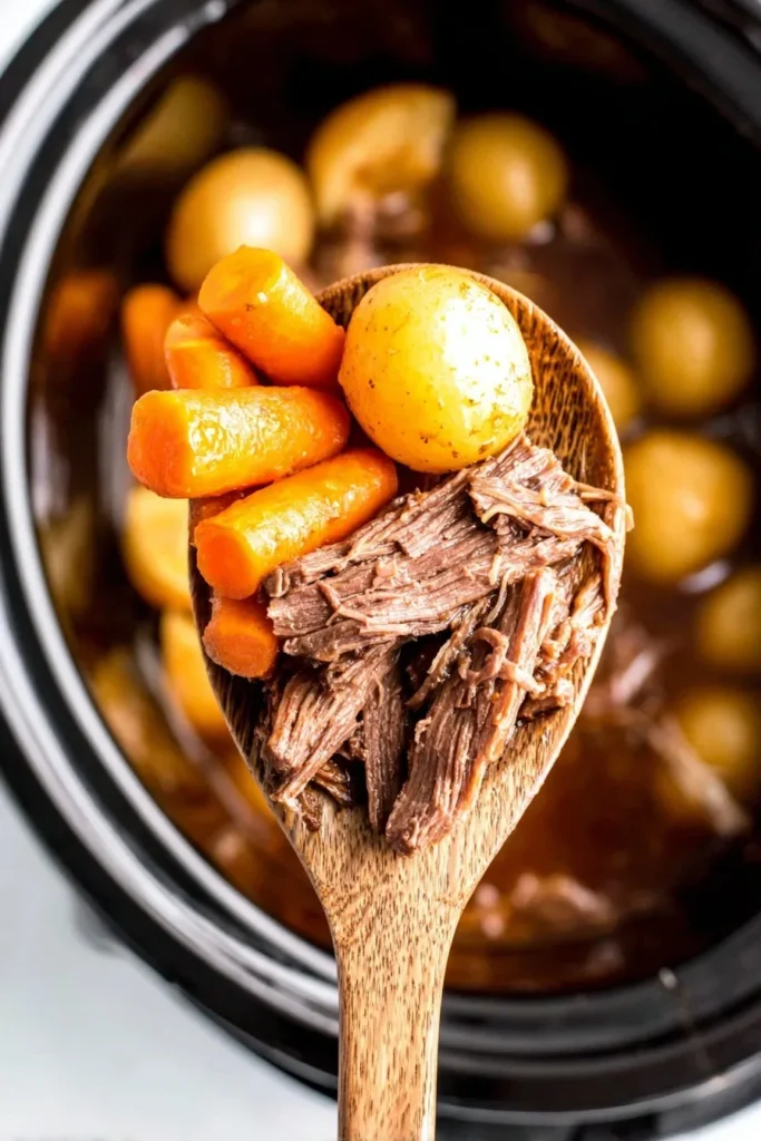 Tender crockpot rump roast with carrots and baby potatoes served on a wooden spoon