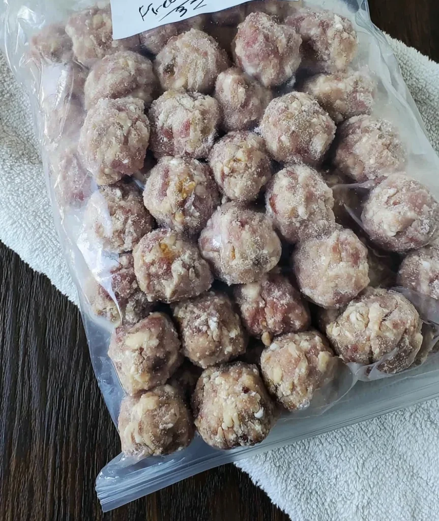 Homemade uncooked frozen meatballs stored in a labeled freezer bag on a kitchen towel