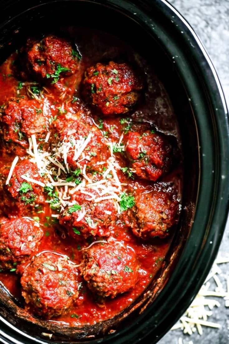 Slow-cooked meatballs in marinara sauce topped with fresh parsley and shredded parmesan inside a black crockpot