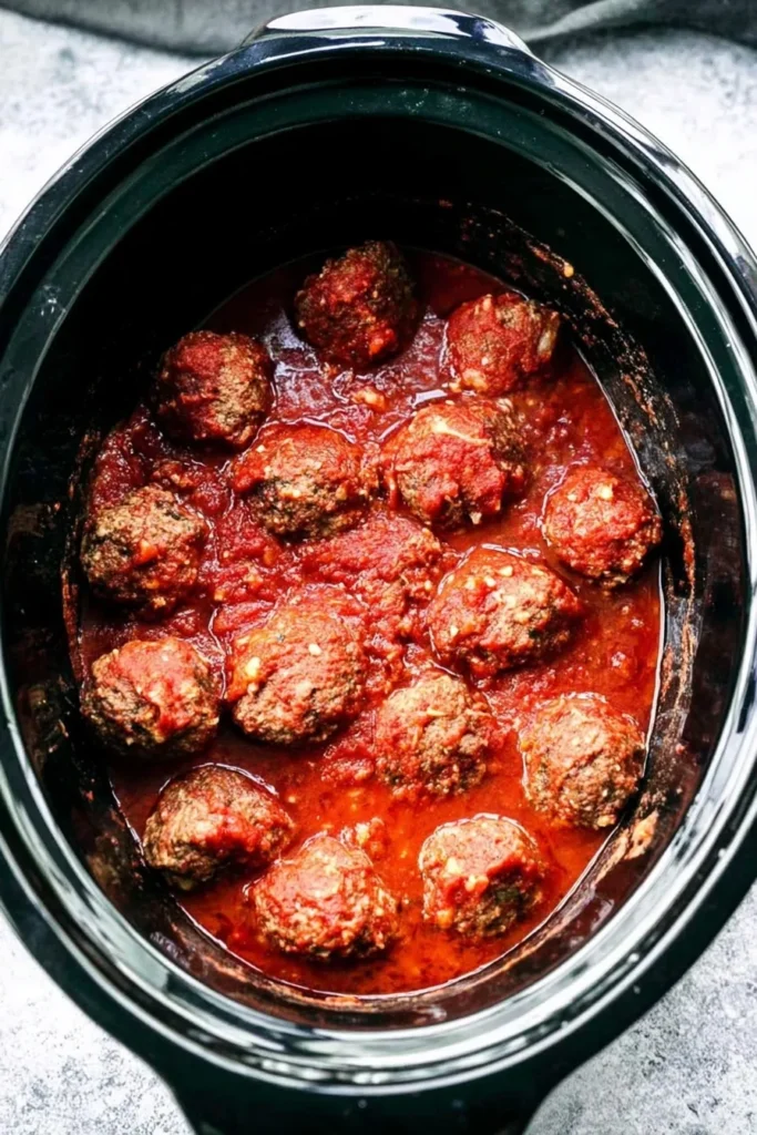 Crockpot Frozen Meatballs simmered in rich tomato sauce inside a black slow cooker