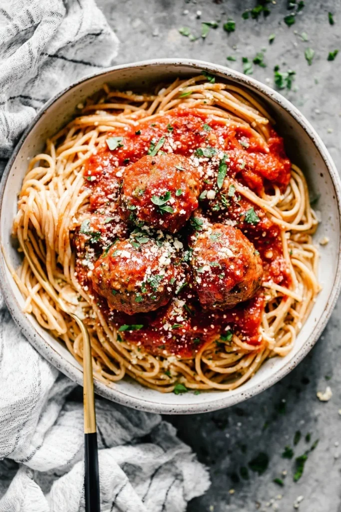 Spaghetti topped with marinara-covered meatballs, parmesan cheese, and parsley served in a rustic ceramic bowl
